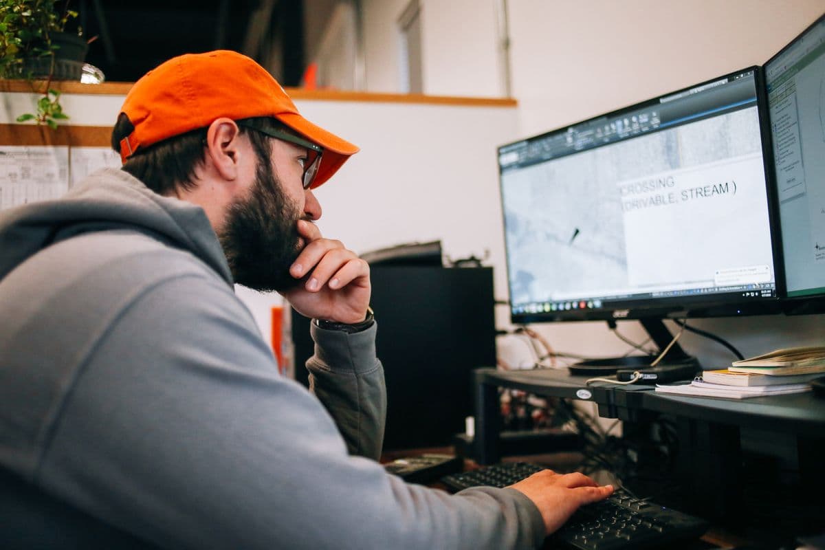 A man in an orange cap studies a site plan on two computer screens at a solar installer's office in upstate New York.