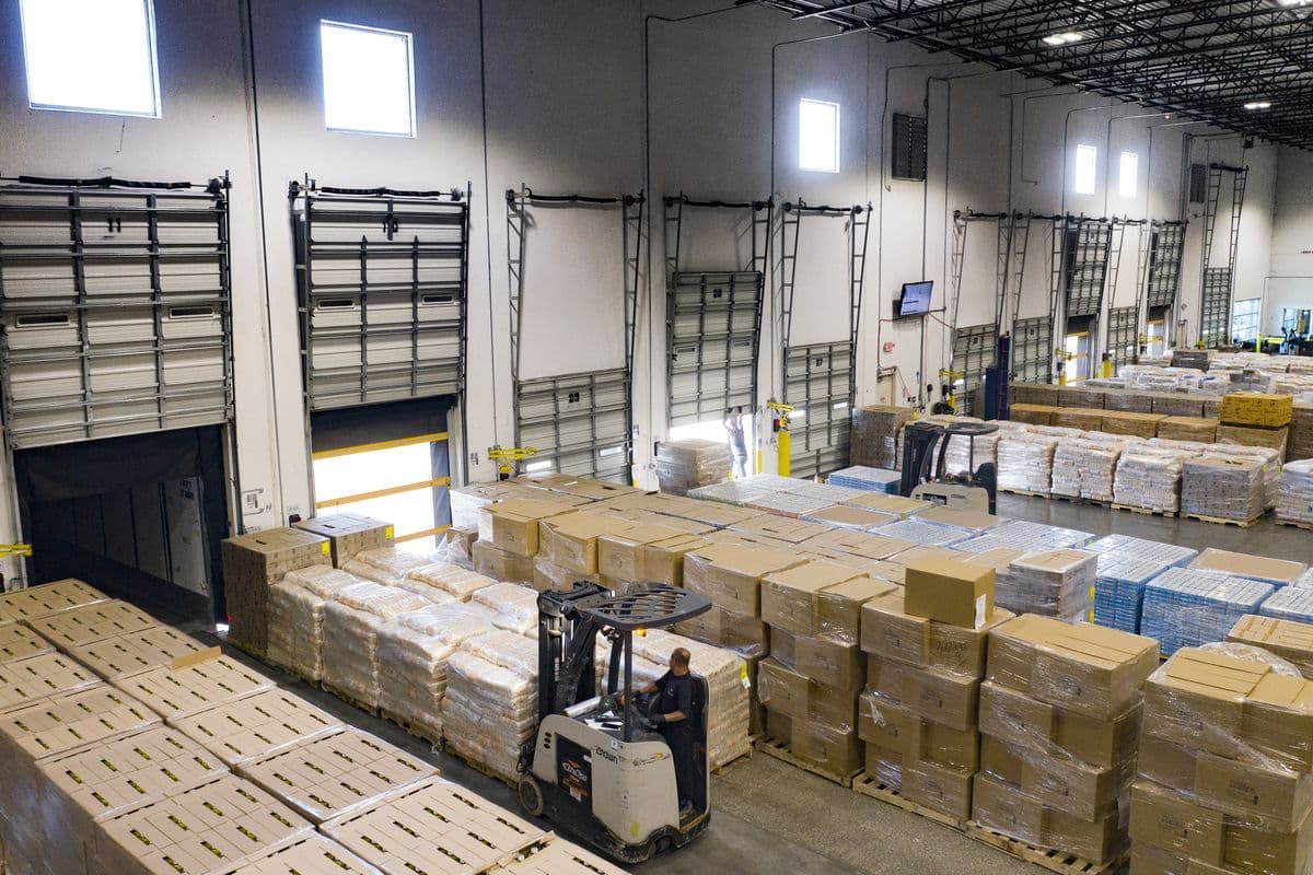 A forklift driver moves among pallets of boxed goods beside loading dock doors in a distribution warehouse in Houston, Texas.